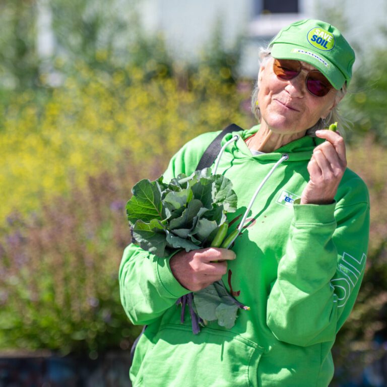 Smiling person holding vegetables with nature in the background.