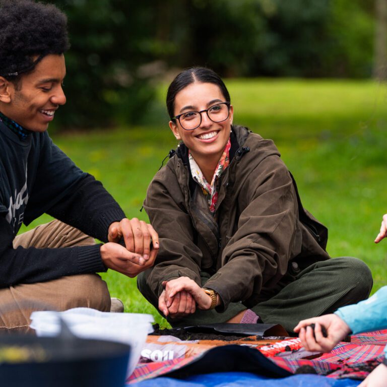 For people sitting outside on a blanket smiling and looking at plants.