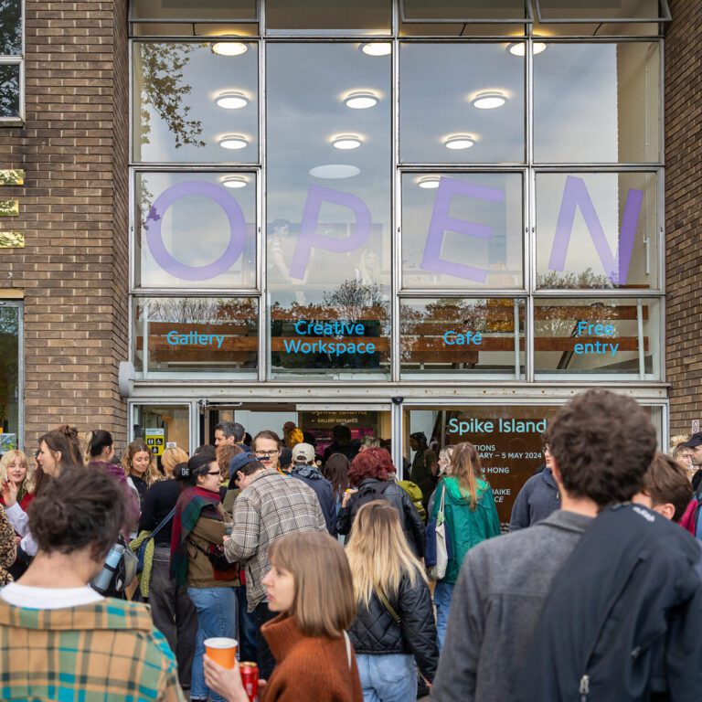 Group of people standing in front of and entering a building with a glass front.