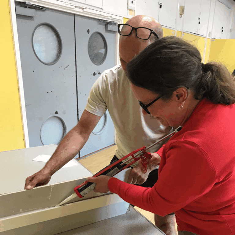 Two people learning how to use caulk in a draught proofing session