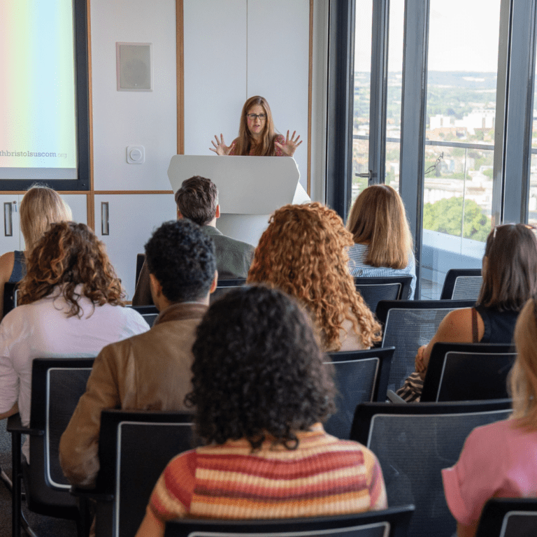 A person speaking at a lectern to a room full of people