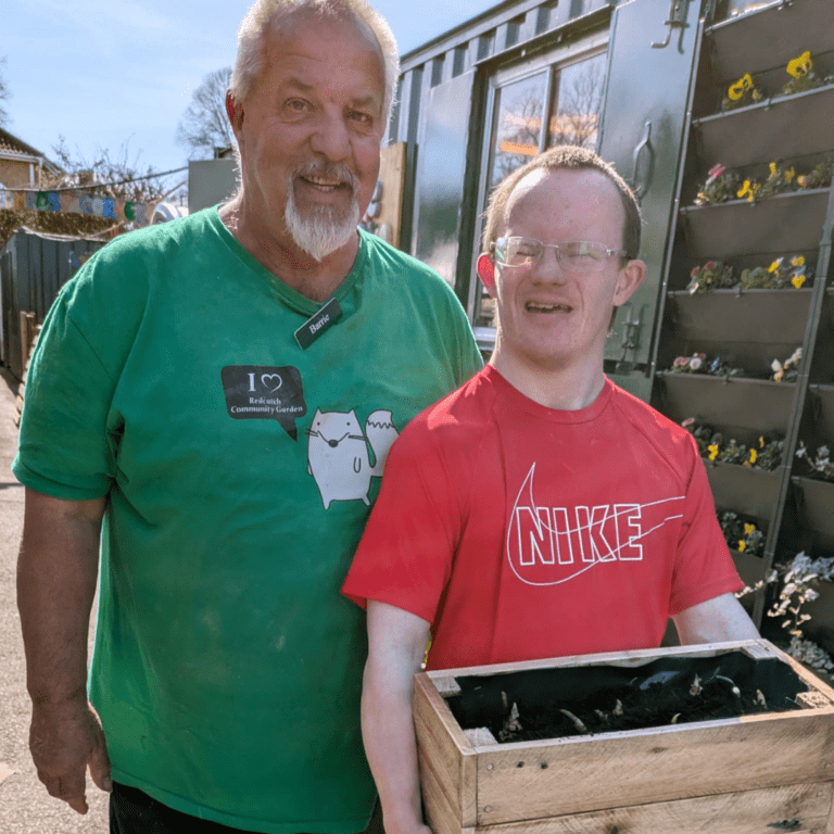 Two men standing together and smiling. One holds a wooden planter.
