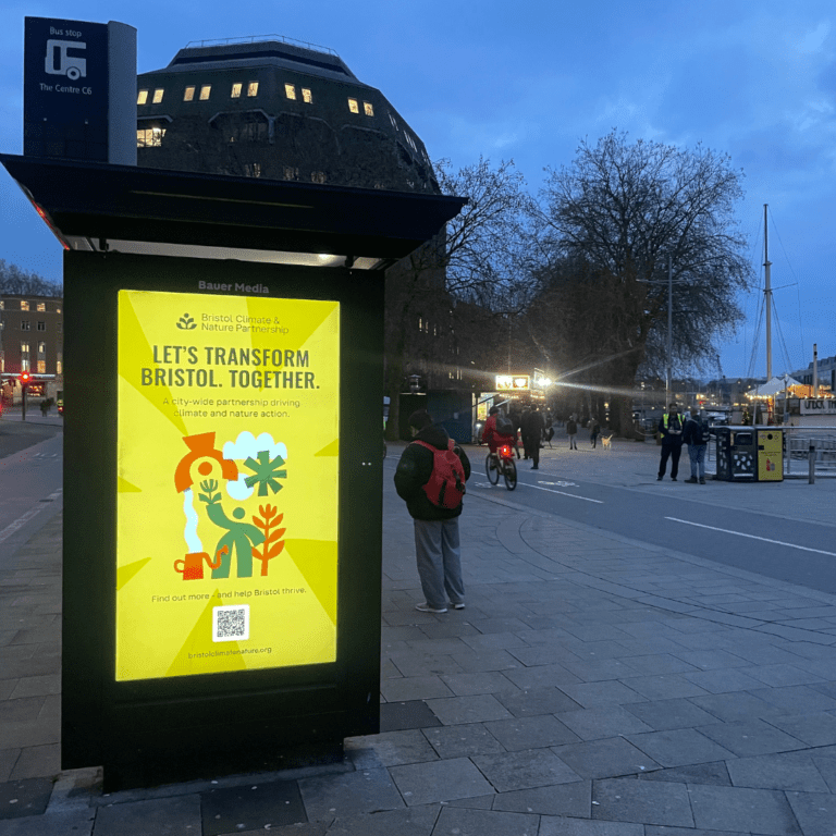 A bus stop at night with a yellow poster on the digital screen. It says 'Let's transform Bristol. Together.'