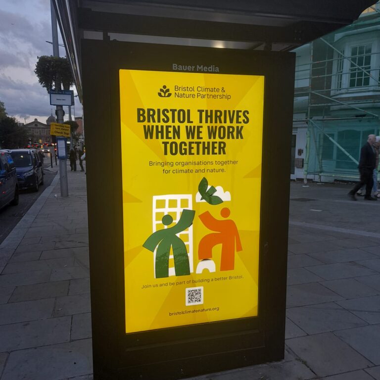 A photo of a digital billboard at dusk in a busy area. It is yellow. It reads 