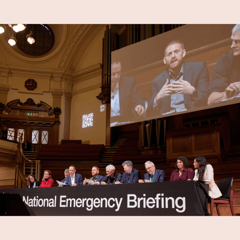 Several people on a panel on stage with banner saying National Emergency Briefing