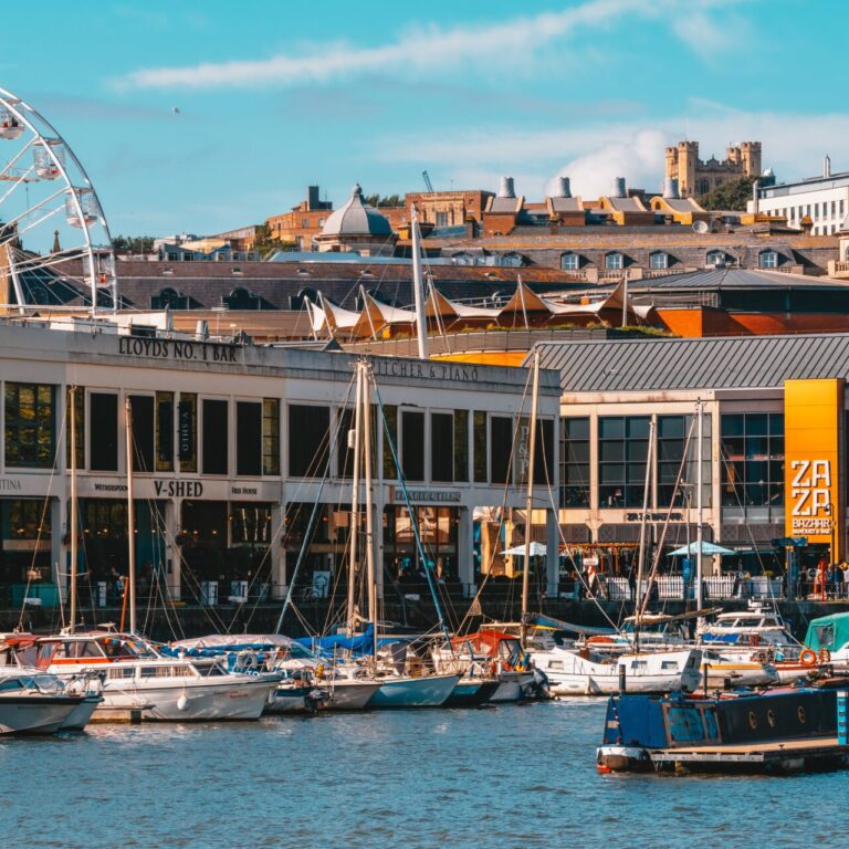 Photo of Bristol Harbourside with water in the foreground and boats and buildings in the background.