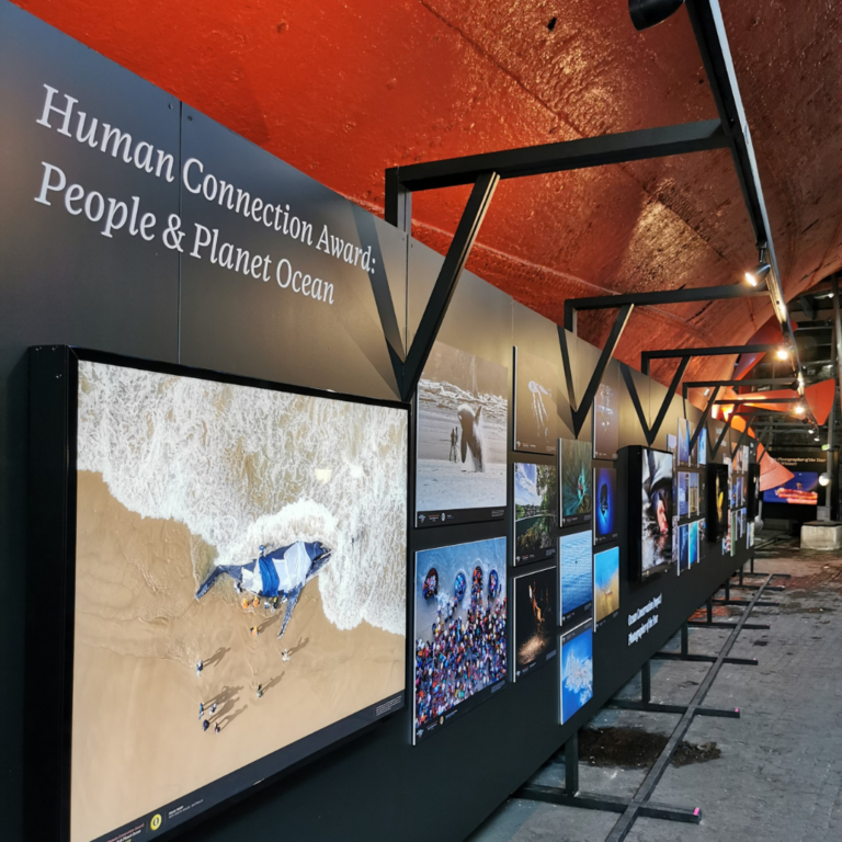 Exhibition stands showing ocean photography in front of the hull of SS Great Britain