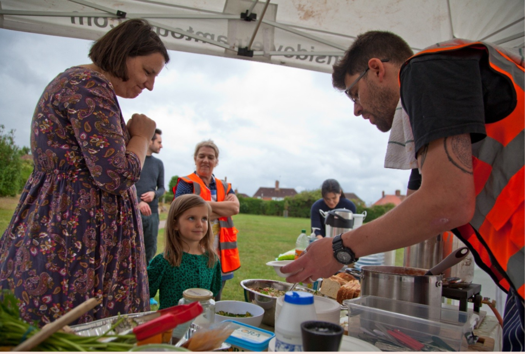 A child being served food at a stall. There are adults standing around. They look happy.